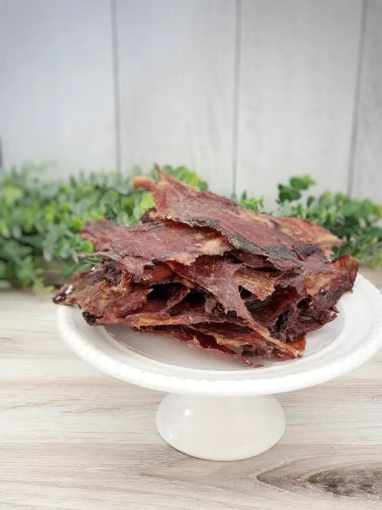 Beef Lips (Fat Trimmed) Thin Cut jerky slices; reddish-brown on a white pedestal plate
