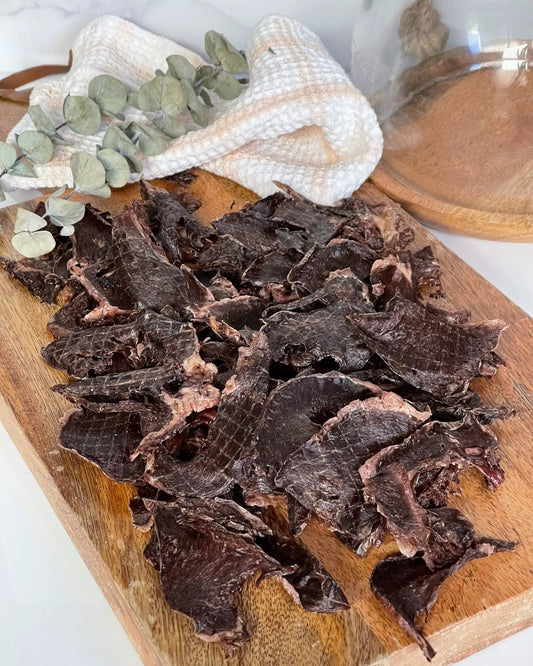 Pork heart thin-cut slices with fat trimmed, dark cured meat on a wooden board with eucalyptus leaves