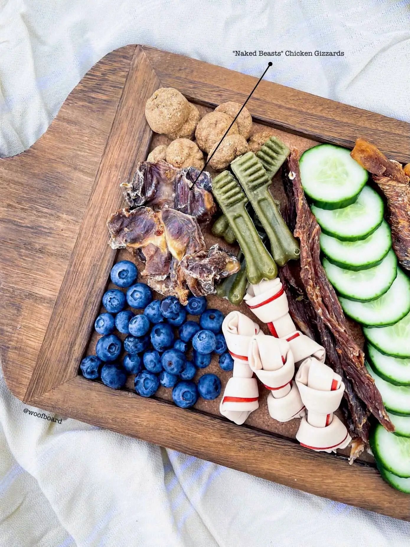 Chicken gizzards by Naked Beasts on a wooden board with blueberries and cucumber slices.