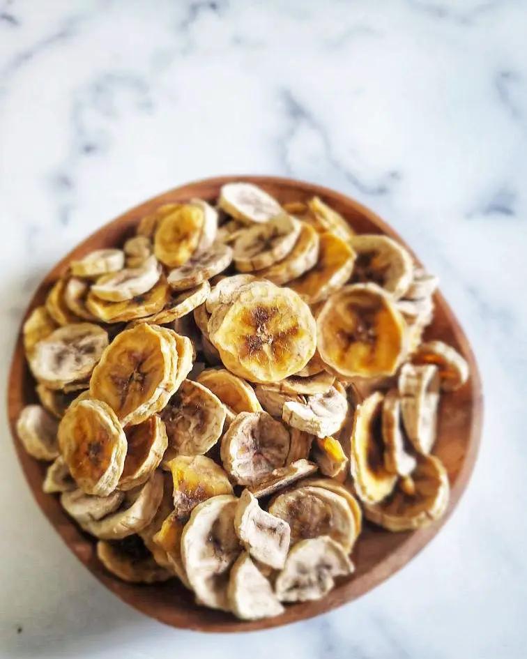 Banana chips by Naked Beasts in a wooden bowl; golden brown dried banana slices.