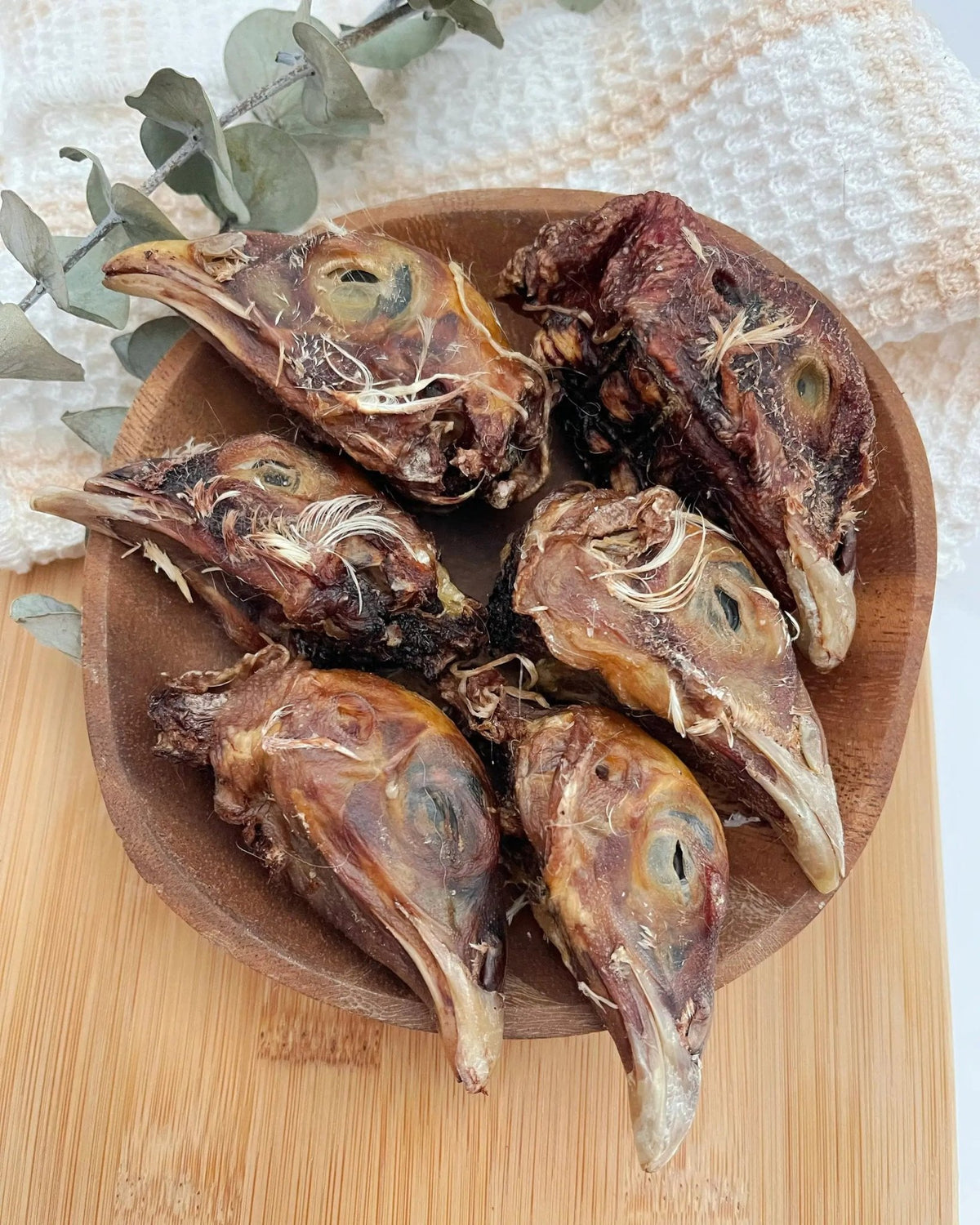 Pheasant Heads by Naked Beasts, roasted game heads in a brown bowl with eucalyptus sprigs.
