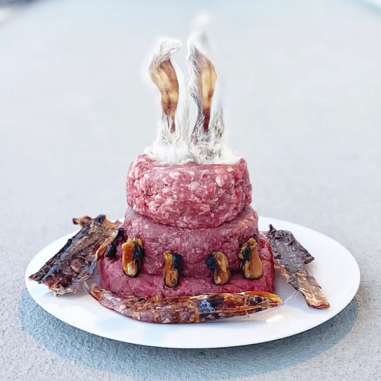 Shrimp by Naked Beasts; two stacked pink ground-meat patties on a white plate with shrimp garnish