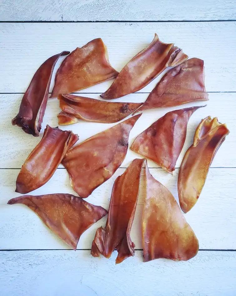 Naked Beasts pig ears, dried pork chews, 12 pieces scattered on white wooden planks