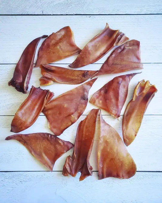 Naked Beasts pig ears, dried pork chews, 12 pieces scattered on white wooden planks