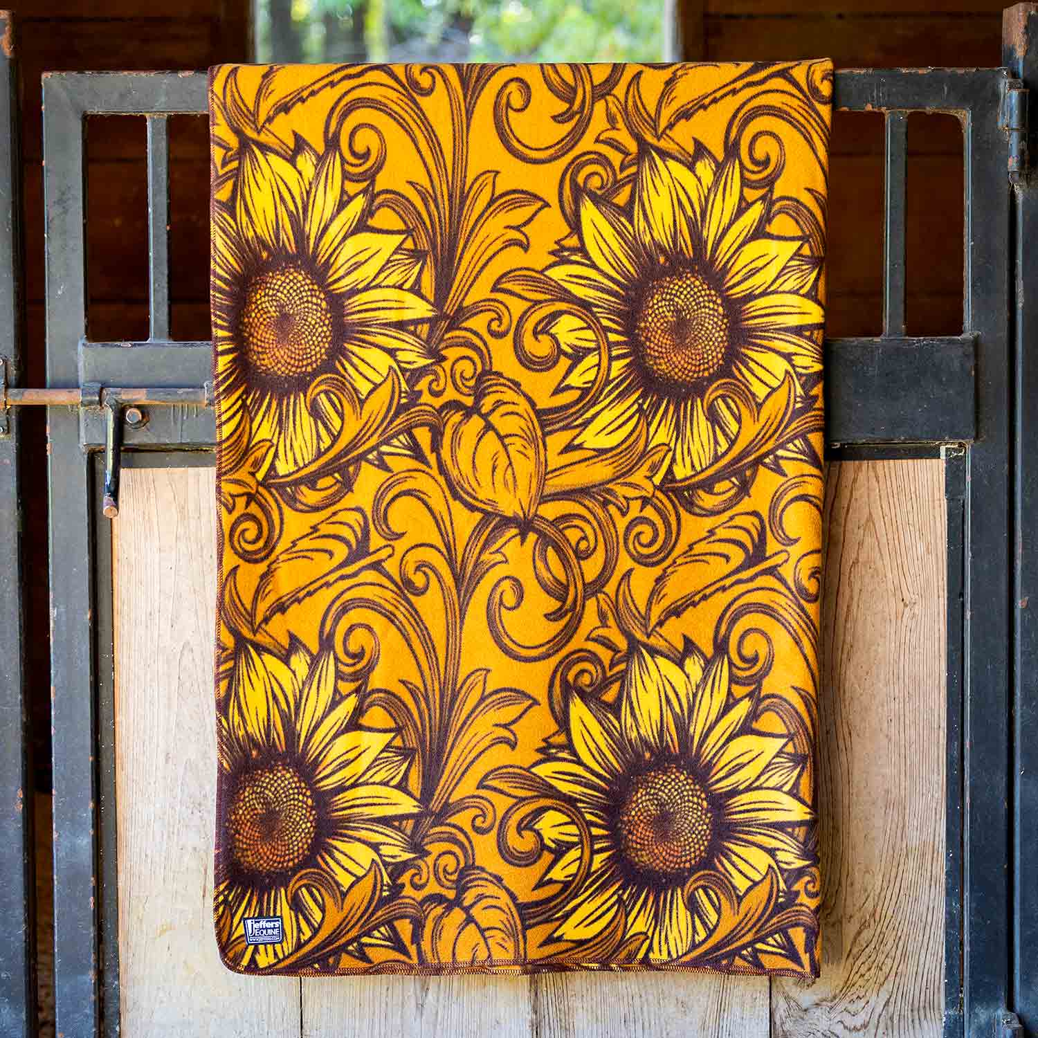 Jeffers Expression oversized fleece throw blanket with sunflower print in yellow and brown; brand label visible.