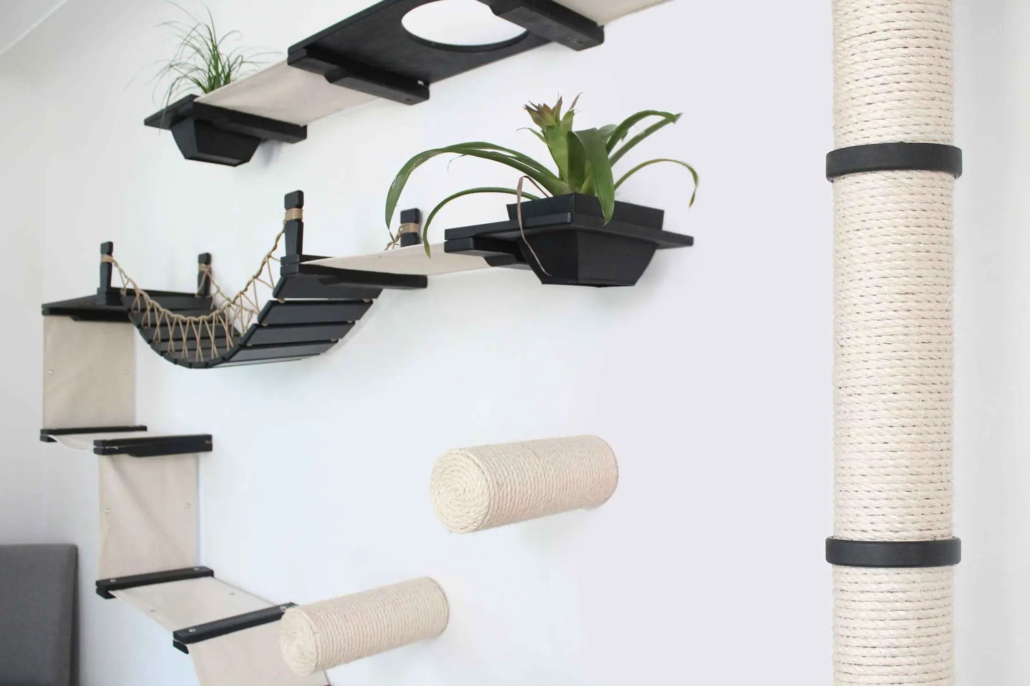 The Juggernaut cat condo on wall by Catastrophic Creations, black platforms with beige elements and a tall sisal post.