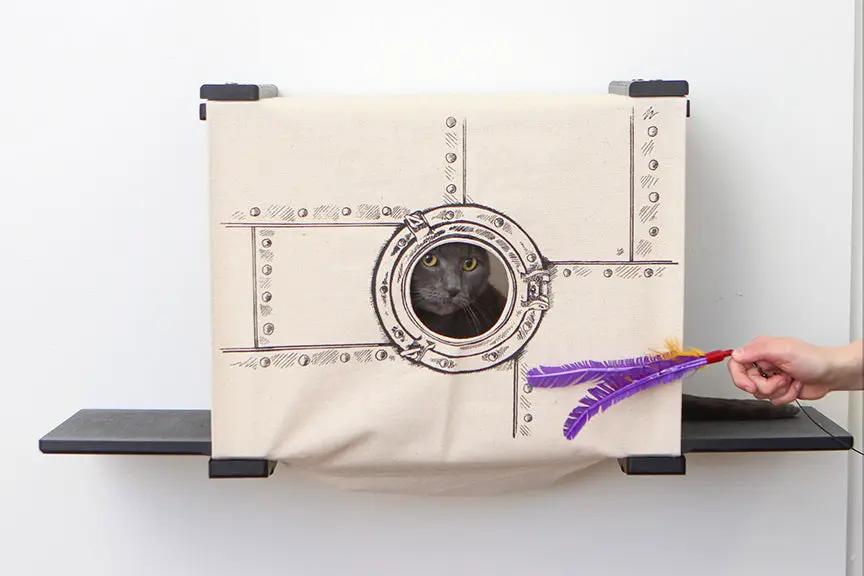 Cat Cubby for Wall - Covered Cat Bed, beige canvas with round porthole entry, cat peeking inside
