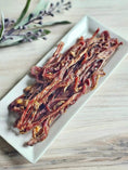 Load image into Gallery viewer, Lamb Pizzle - Limited Edition by Naked Beasts on a white plate; dried, twisted meat strips.
