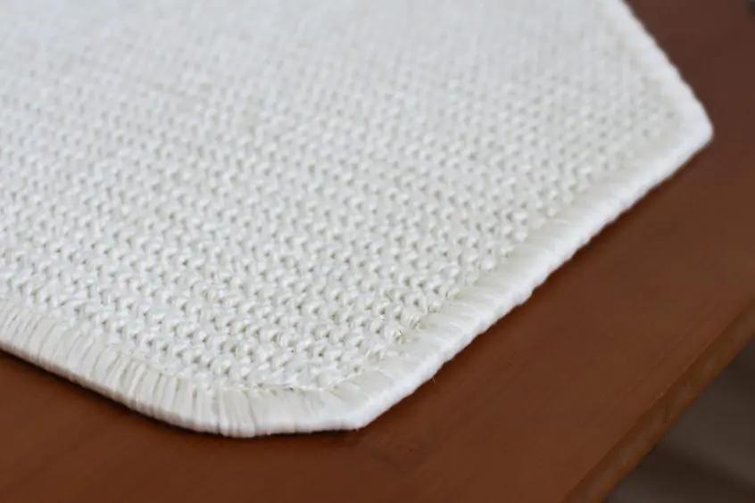 The Overlook cat condo by Catastrophic Creations, white woven mat with fringed edge on wood surface